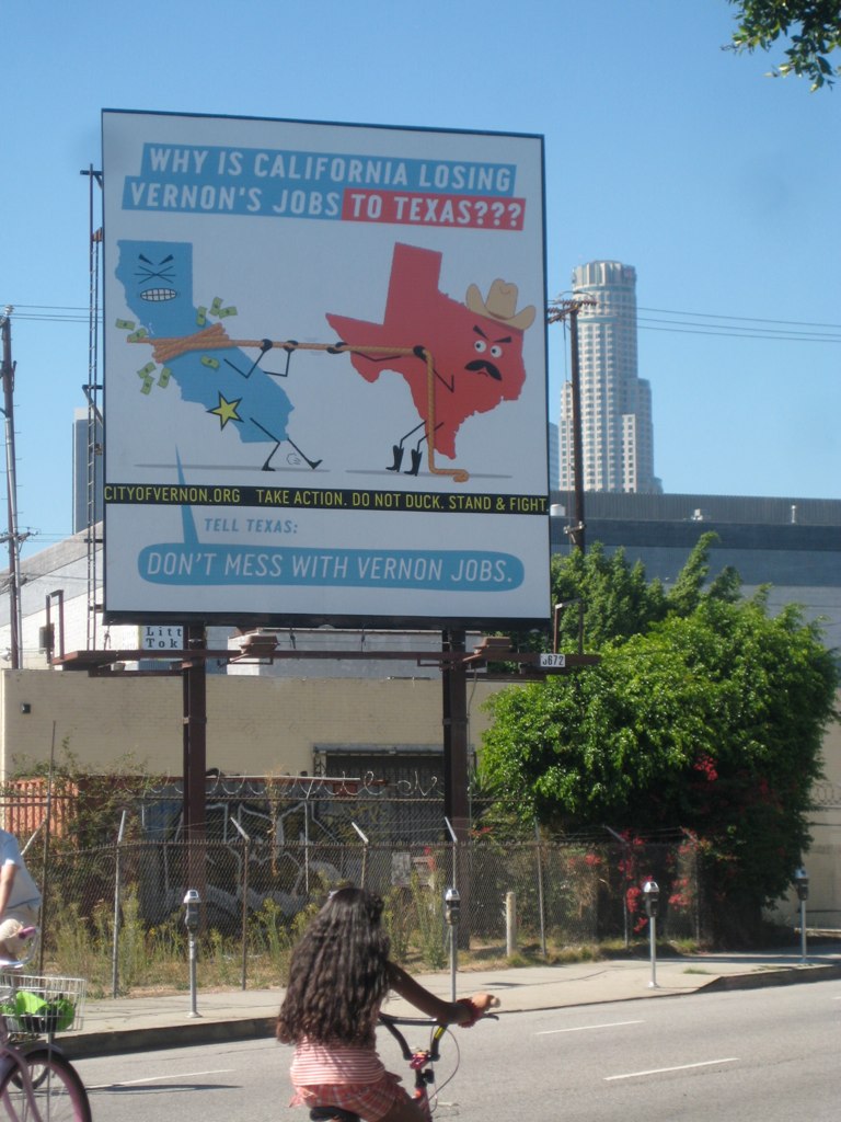 a billboard saying, why is california losing vernon's job to texas? on a street corner
