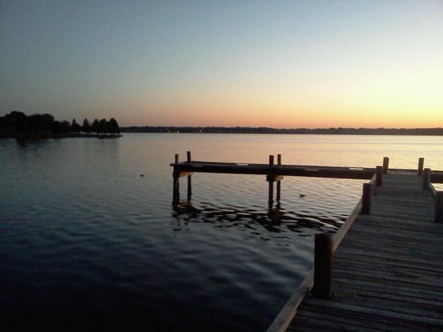 an empty pier sitting on the side of a lake at dusk