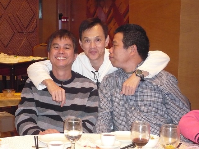 two men, one man has his arms around another man who is sitting at a table