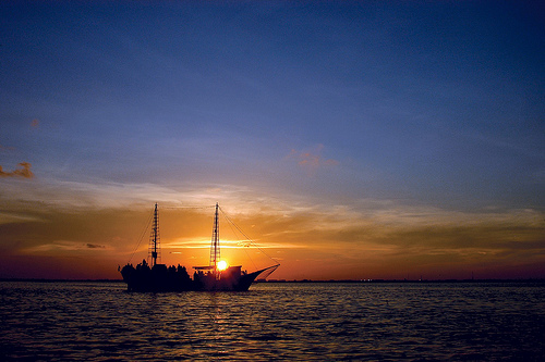 an old ship sitting in the water as the sun goes down
