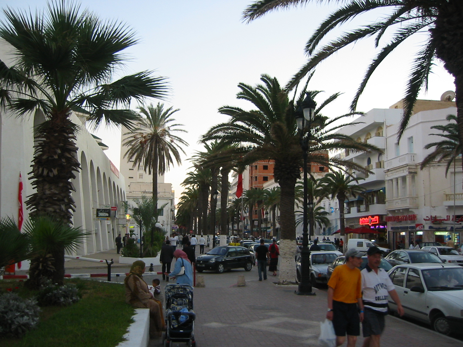 people on a sidewalk with cars and palm trees
