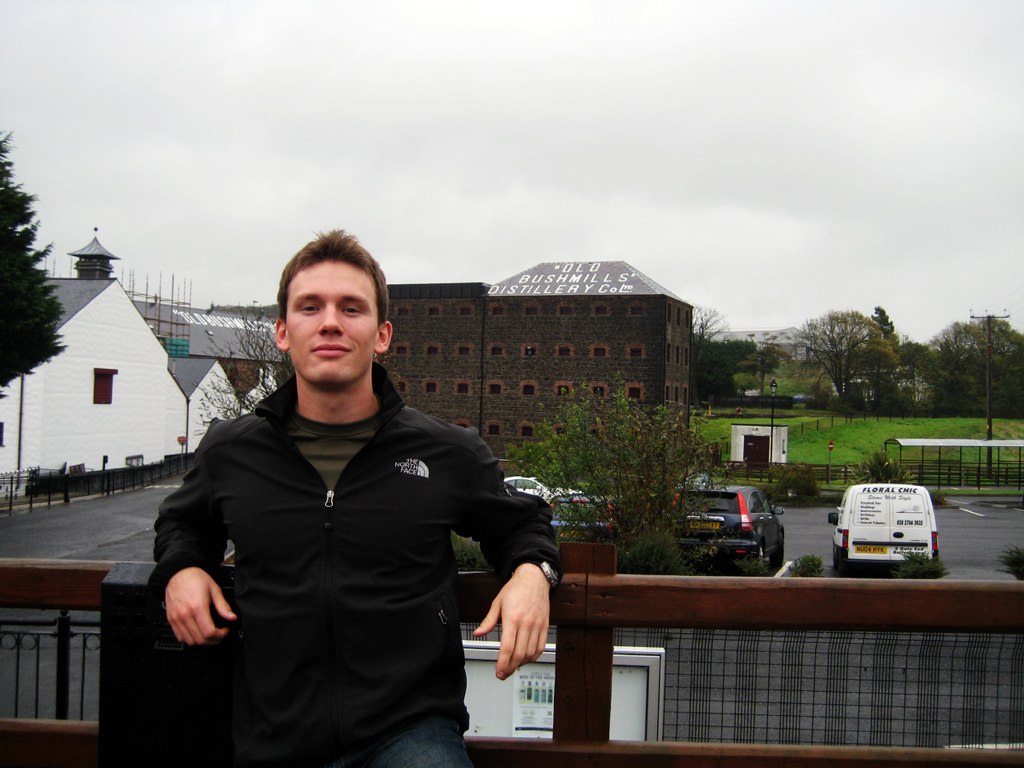 a man poses in front of the camera with buildings behind him