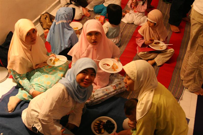 several women and children sitting on the floor eating together
