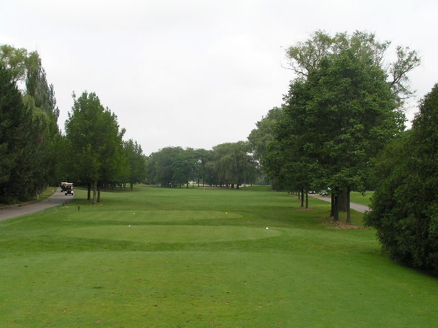 an empty, grassy, park - like golf course with a cart parked in the background