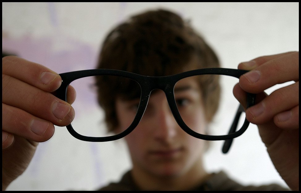 young adult person trying out black eyeglasses with his eyes