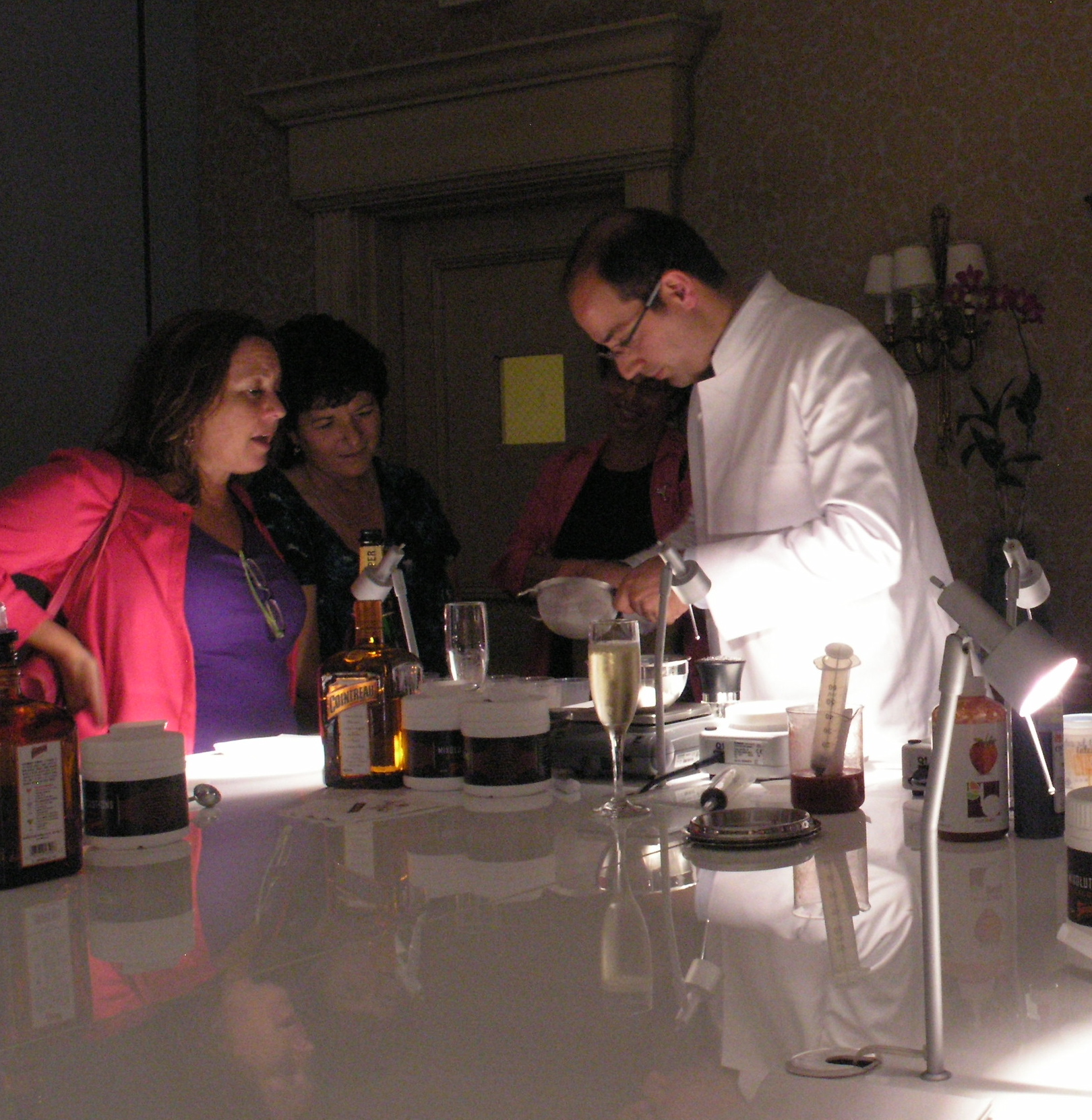 the man in the white suit is pouring drinks at a glass counter