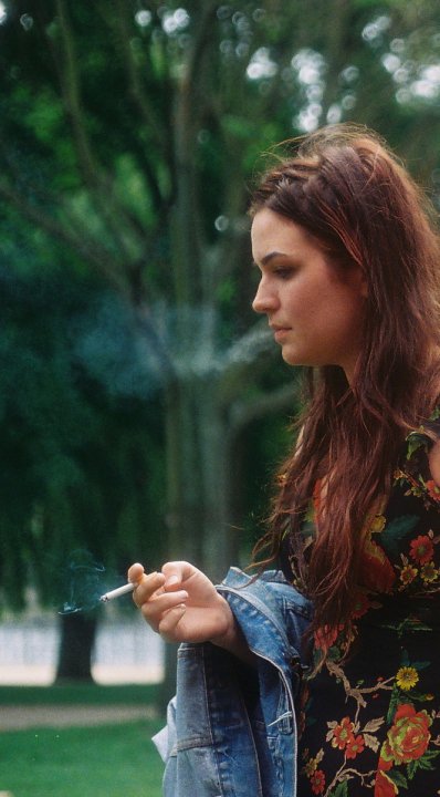 young woman smoking cigarette standing in grassy area