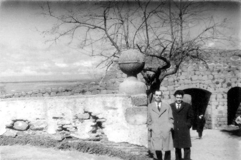 two men stand near a large stone wall