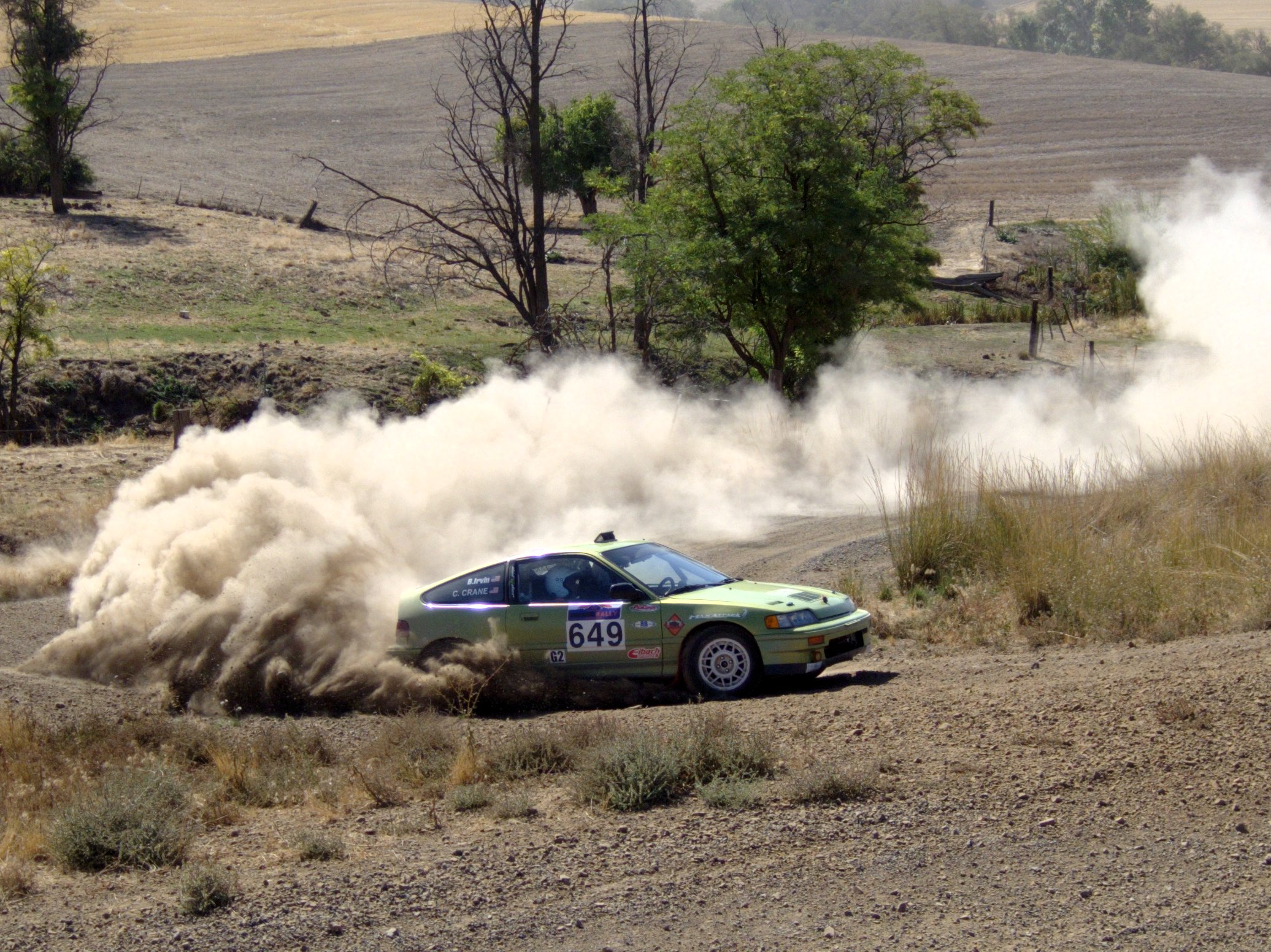 a green rally car kicking up dirt during a race