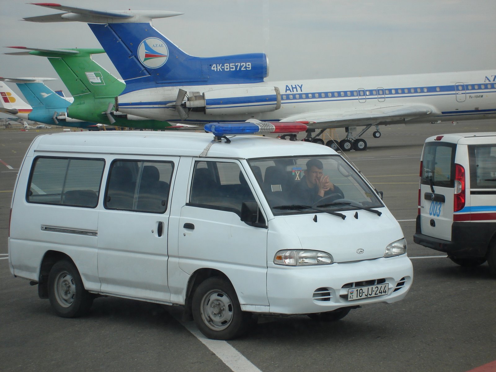 a small white van driving down a runway next to an airplane