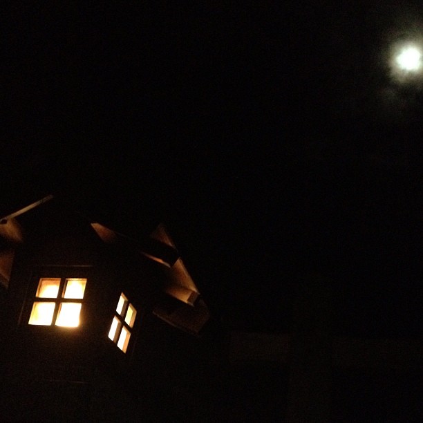 the moon shining through a dark window over a roof