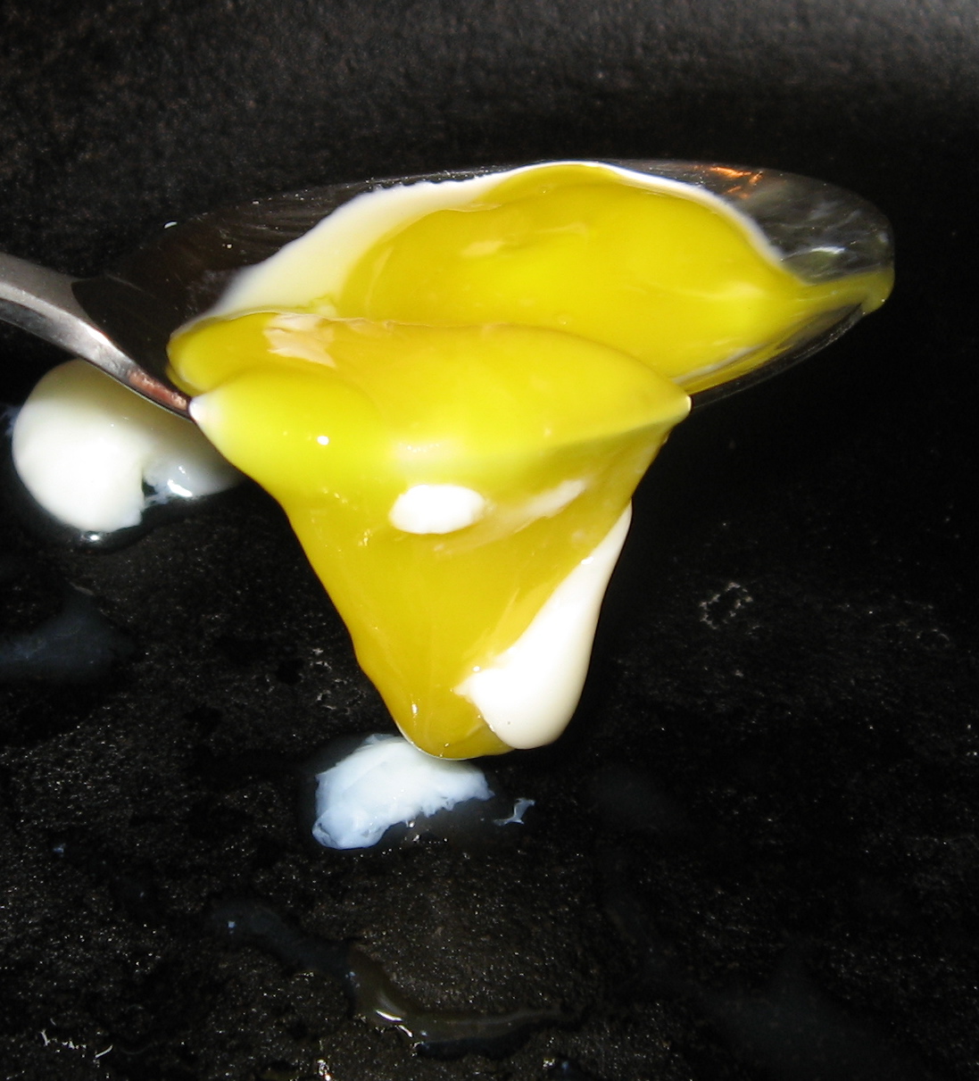spoon pouring melted cheese on black surface for cooking