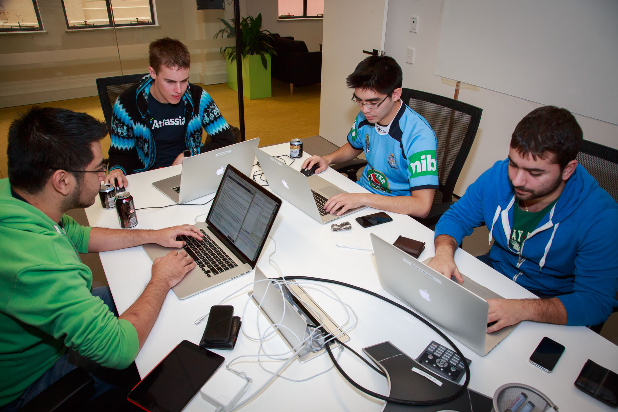 four men sitting at a table using laptops