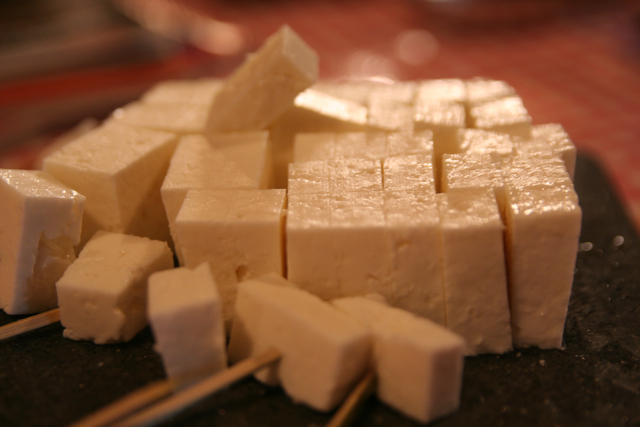 several chunks of cheese on a chopstick and an uncooked block of tofu