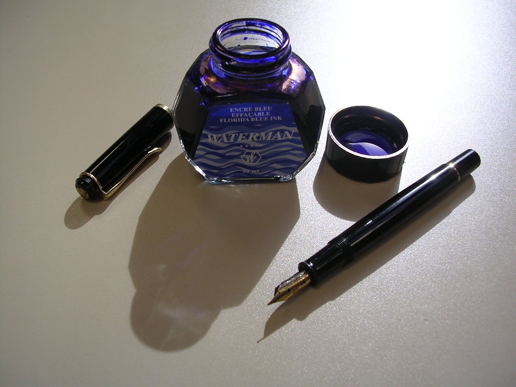a blue fountain pen sitting next to a bottle of ink