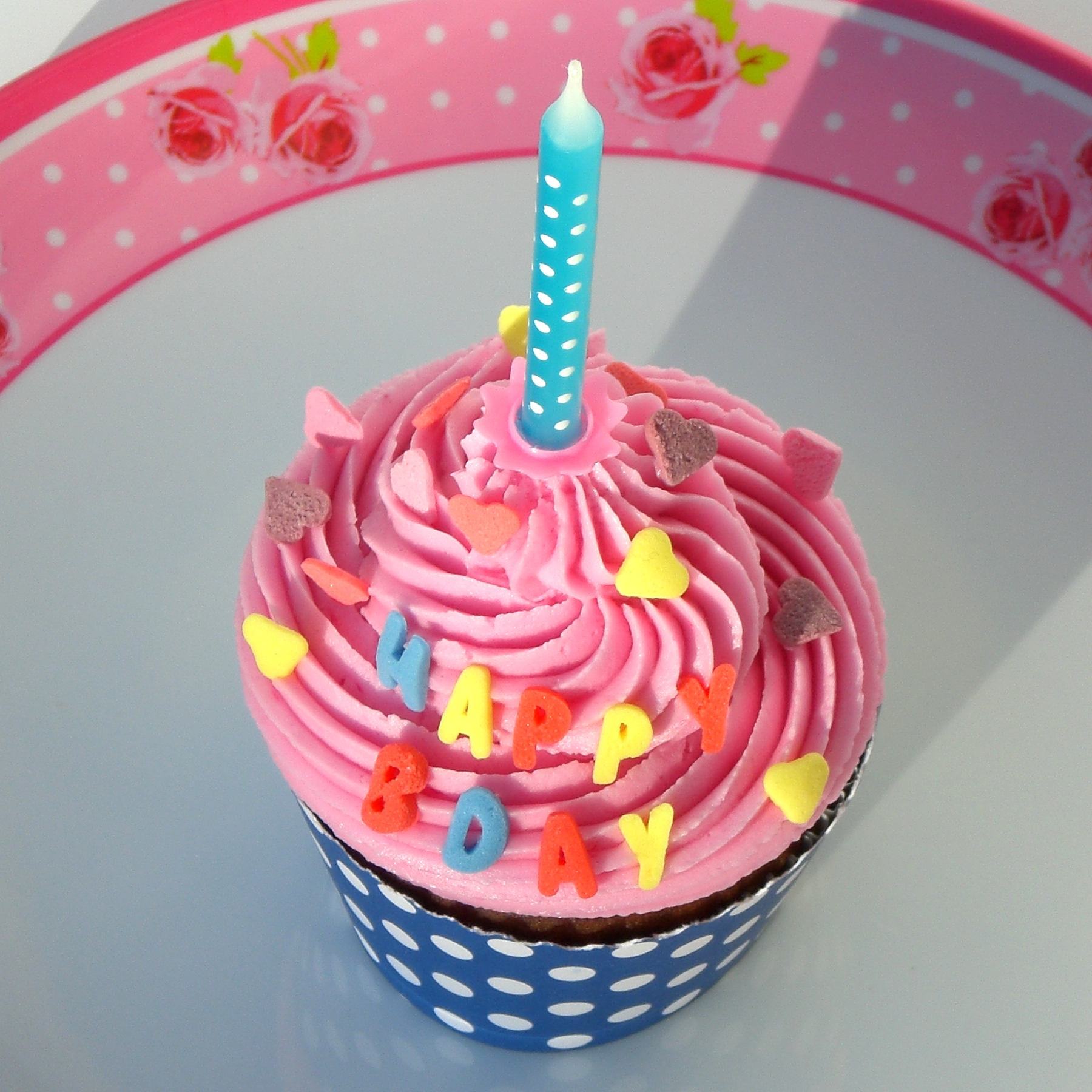 a pink cupcake topped with a lit candle sitting in front of a pink wall