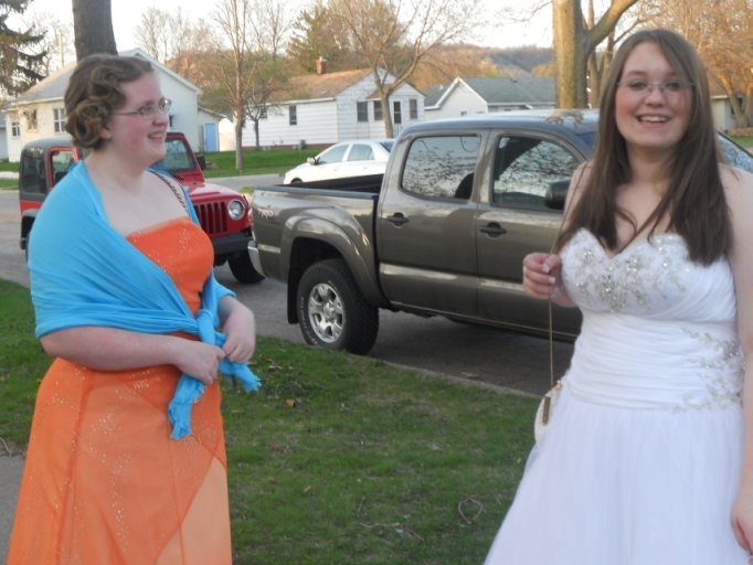 two women dressed in prom attire standing near a house