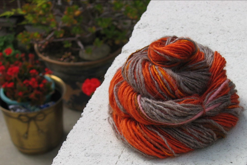 a ball of orange and grey yarn sitting next to potted flowers