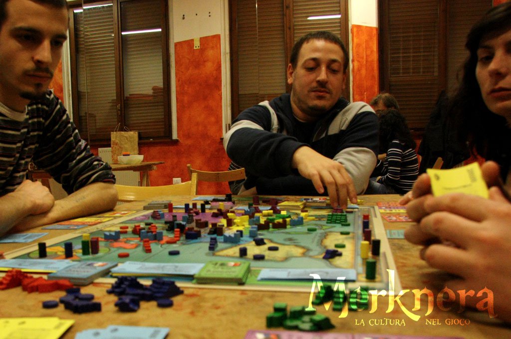 men sitting at a table playing a game with colorful pieces