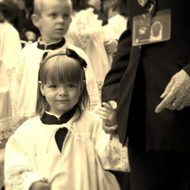 a little girl stands near a priest and other children