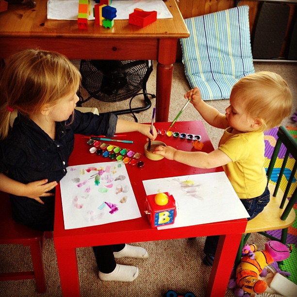 two children sitting at a table in a room playing