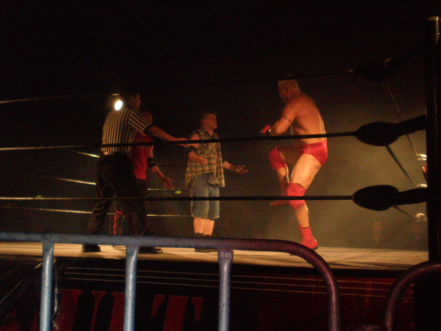 three men with boxers in a ring at night