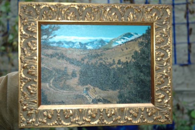 a gold frame holding up a small painting of a mountainside scene