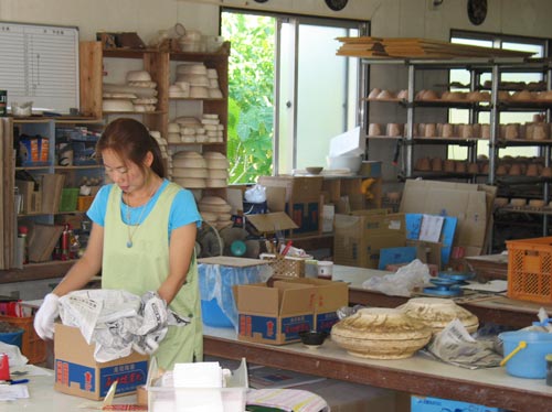 an asian woman sorting through boxes in a large workshop