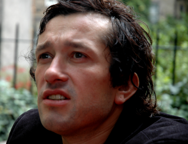 a young man with wet hair wearing a black shirt looking off into the distance