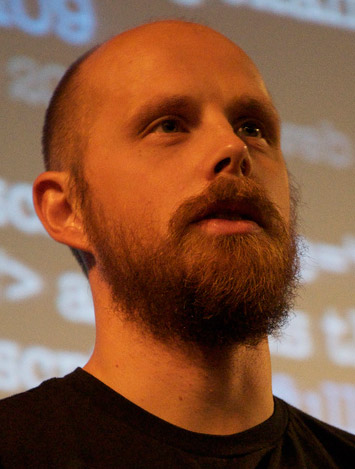 bearded man standing in front of projection screen with red mustache