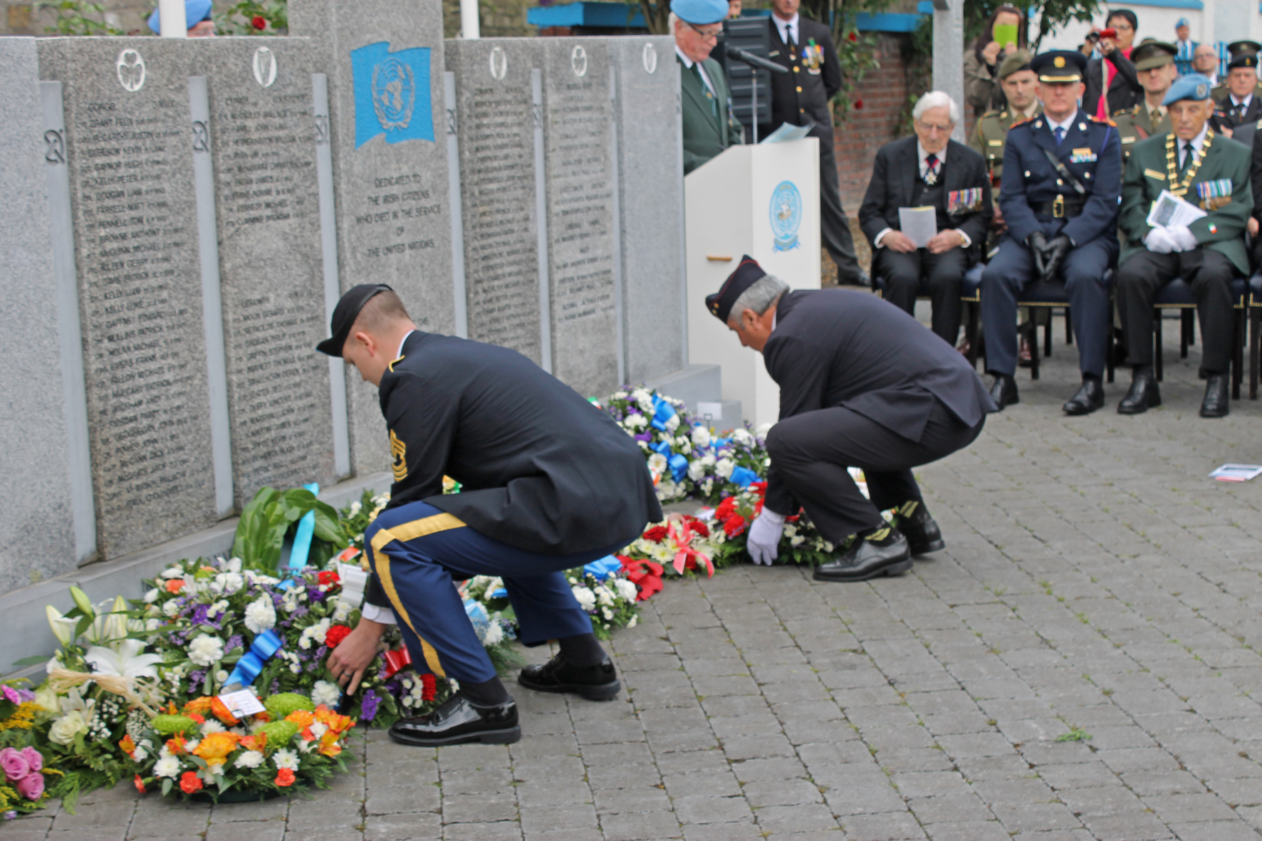 two men kneeling on the ground with wreaths laid on them