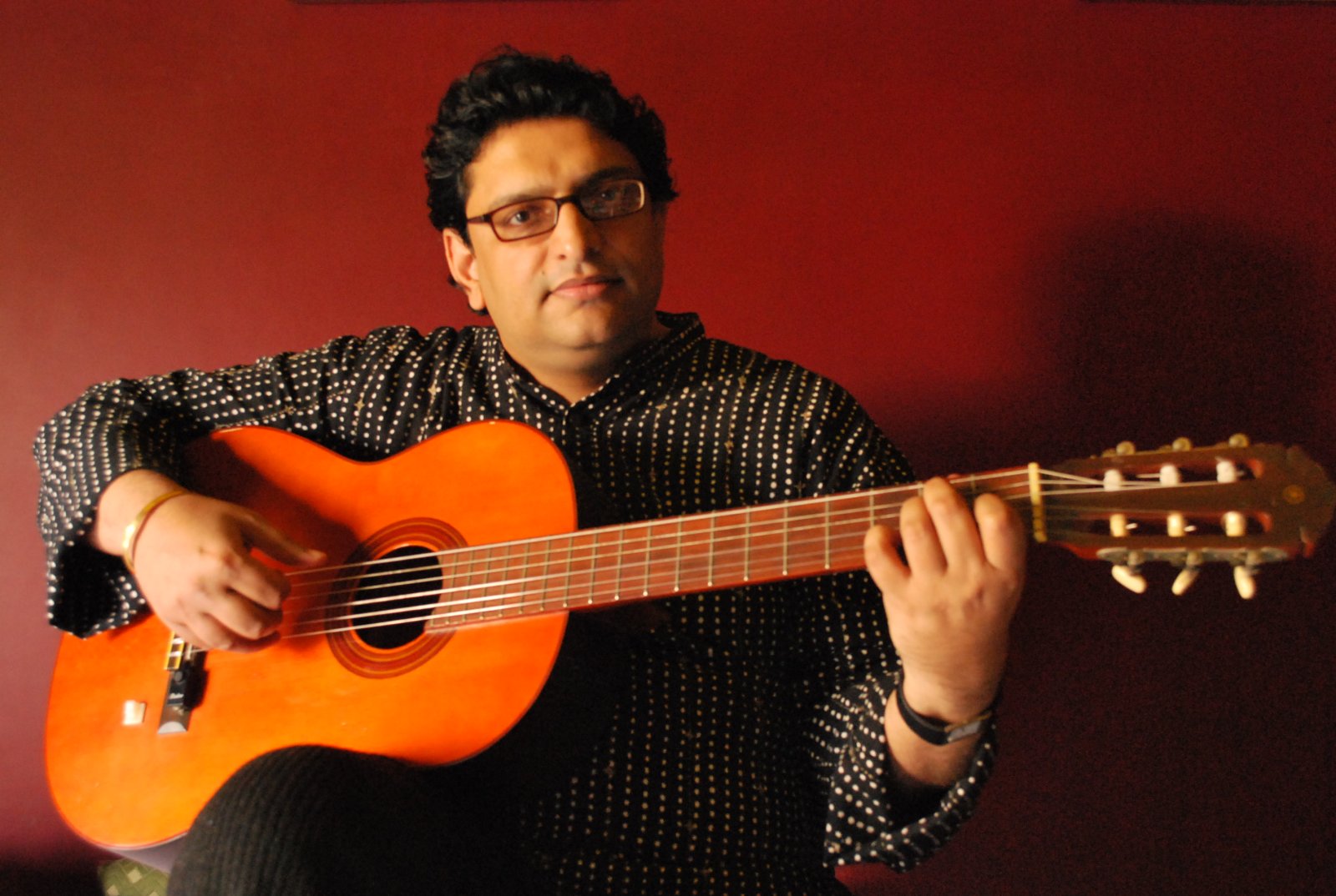 man in glasses is holding an orange guitar and smiling