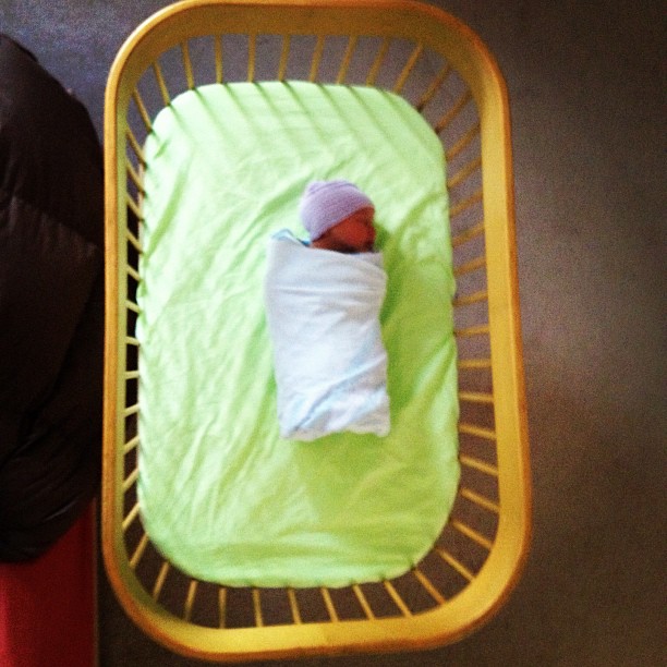 a baby lying in a baby cot on the floor