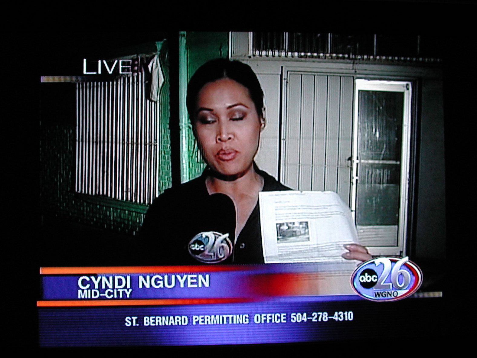 the tv screen shows a news reporter and the newspaper is in her hand