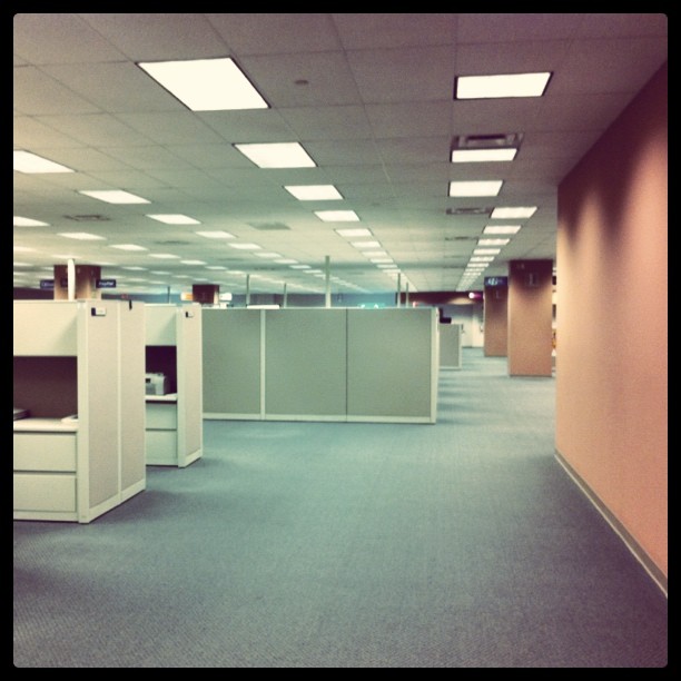 an empty cubicle with two television screens and two file cabinets