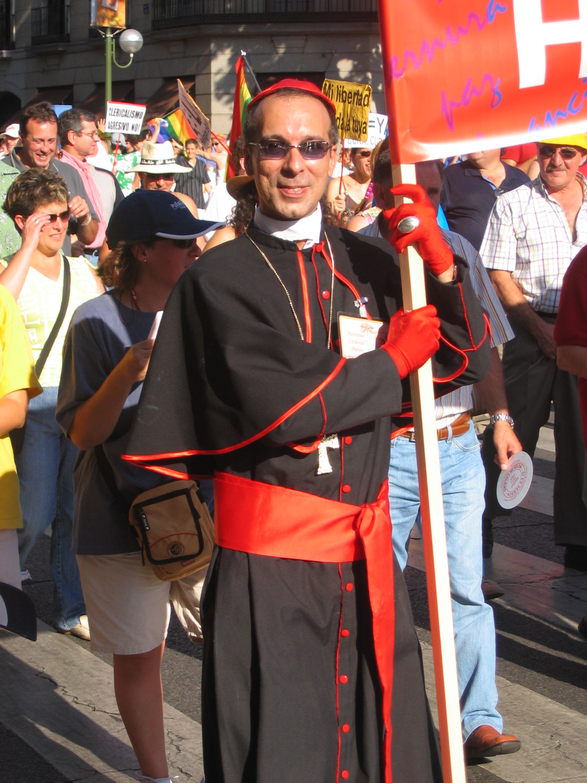 a priest carrying a sign in the street as people watch