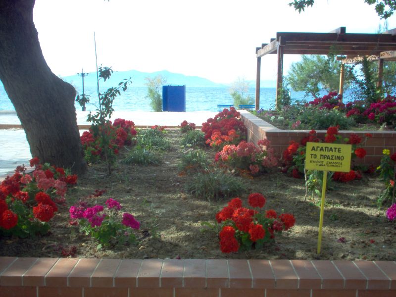 a park with a sign in the middle of it next to some flowers and trees