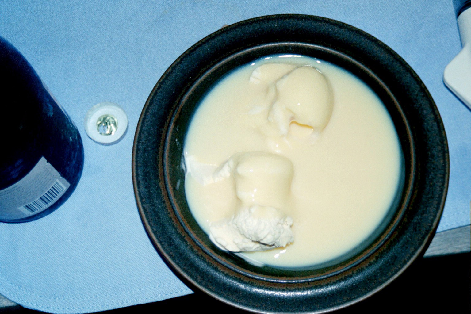 a bowl of cream soup sits next to a bottle of beer