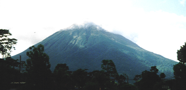 a large, triangular mountain rises above trees and bushes