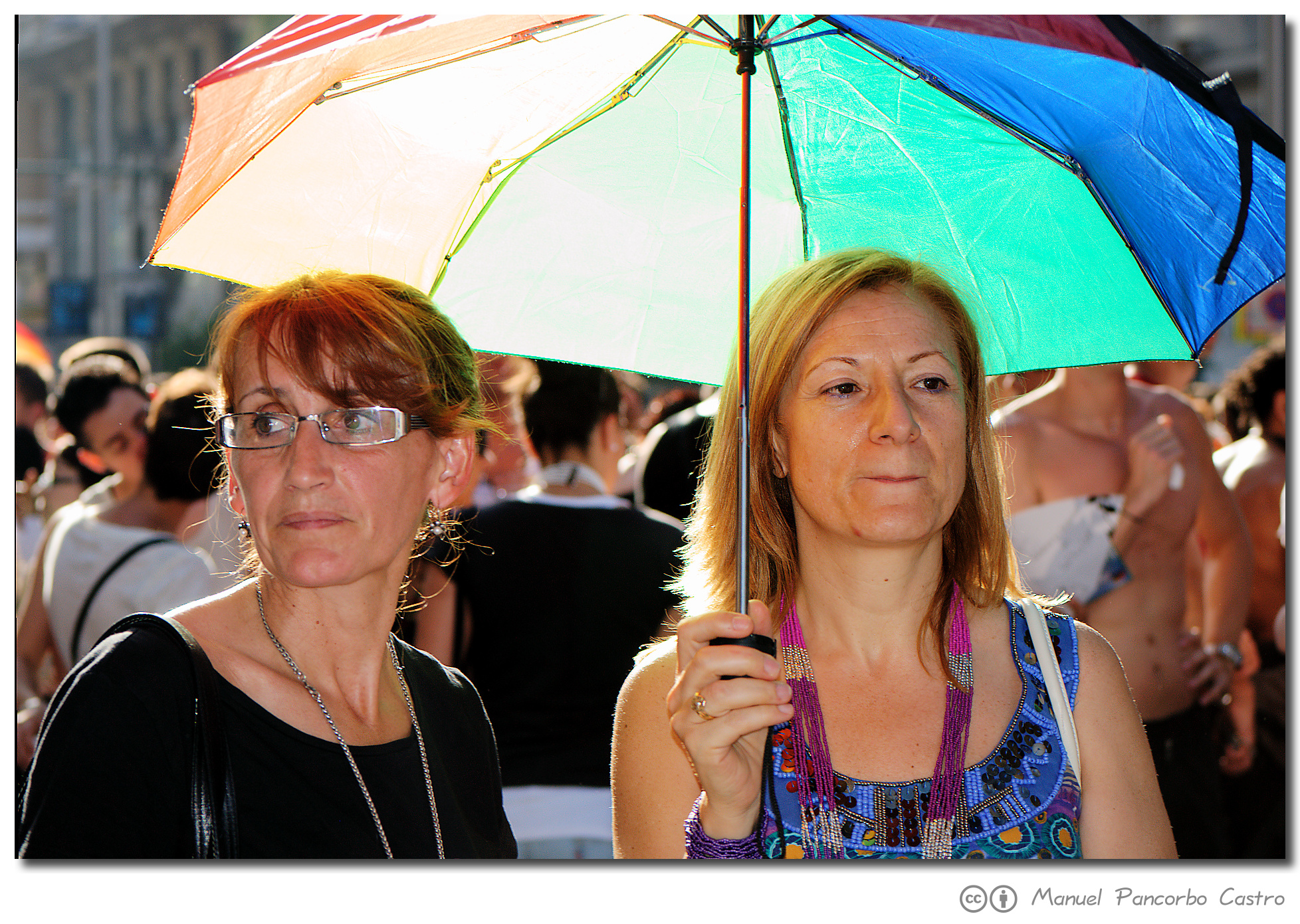 two woman standing under an umbrella in a crowd