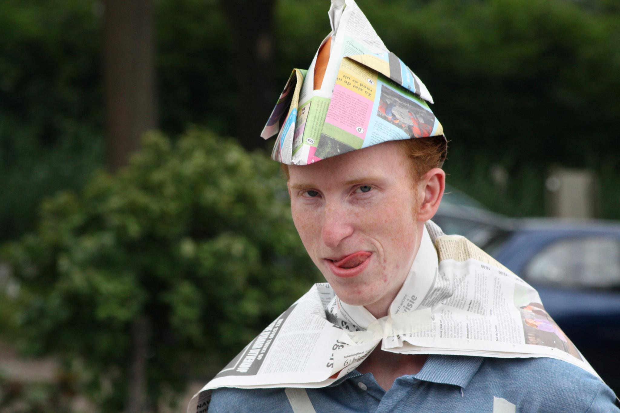 the young man wears a paper party hat while wearing newspaper