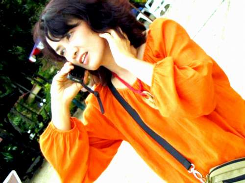 a woman holding a cell phone to her ear while wearing an orange dress