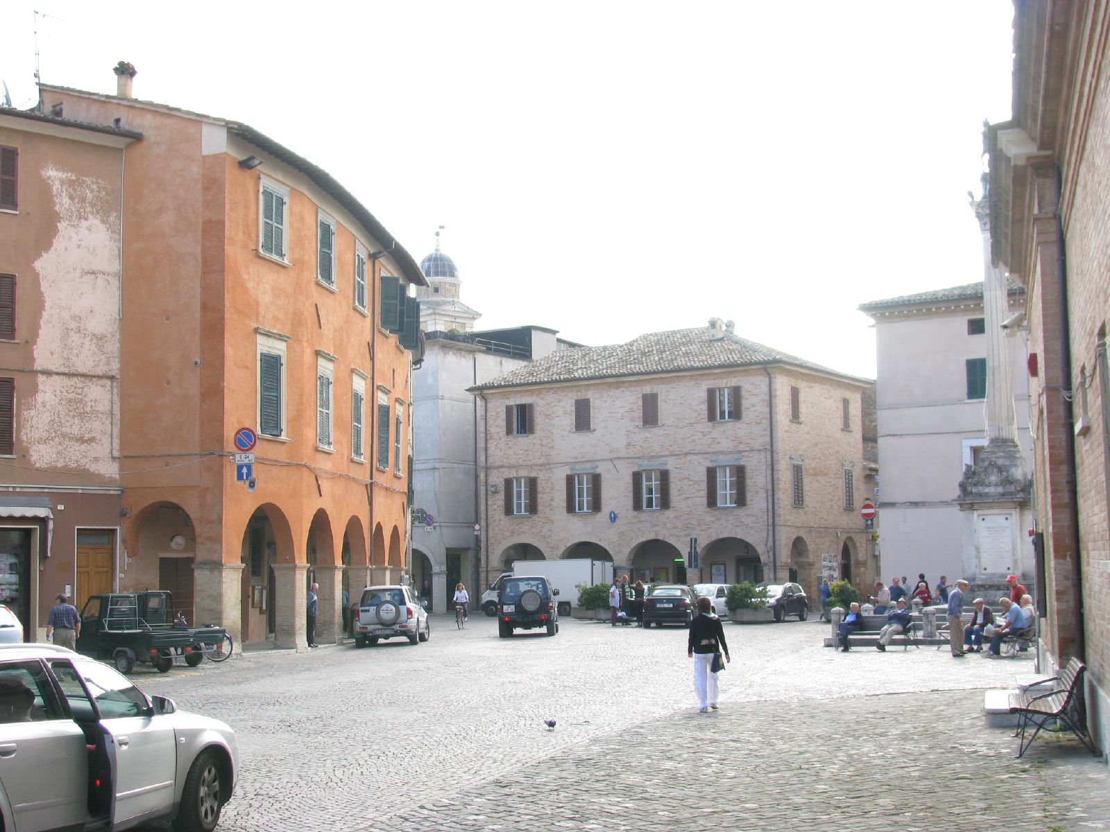 many people in town with parked cars on the street