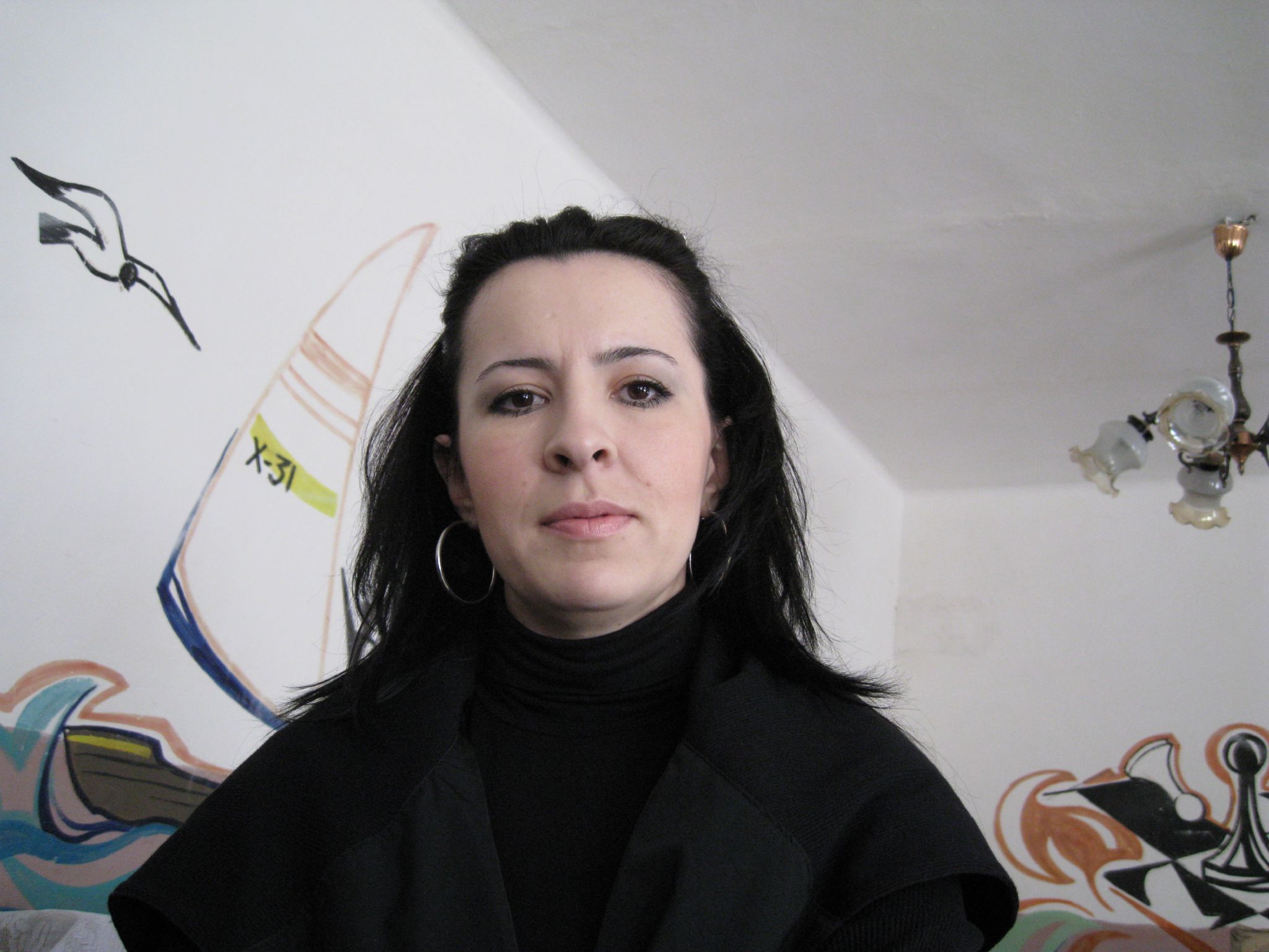 the woman has long hair and black clothing in front of a wall with paintings