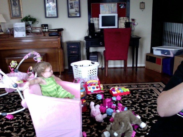 a little girl in green playing with her doll in the living room