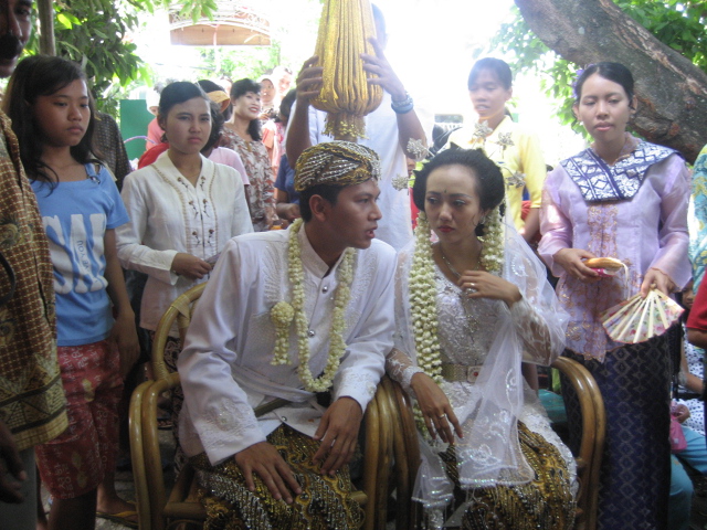 a man and woman in traditional malaysian costumes, sit side by side on a patio
