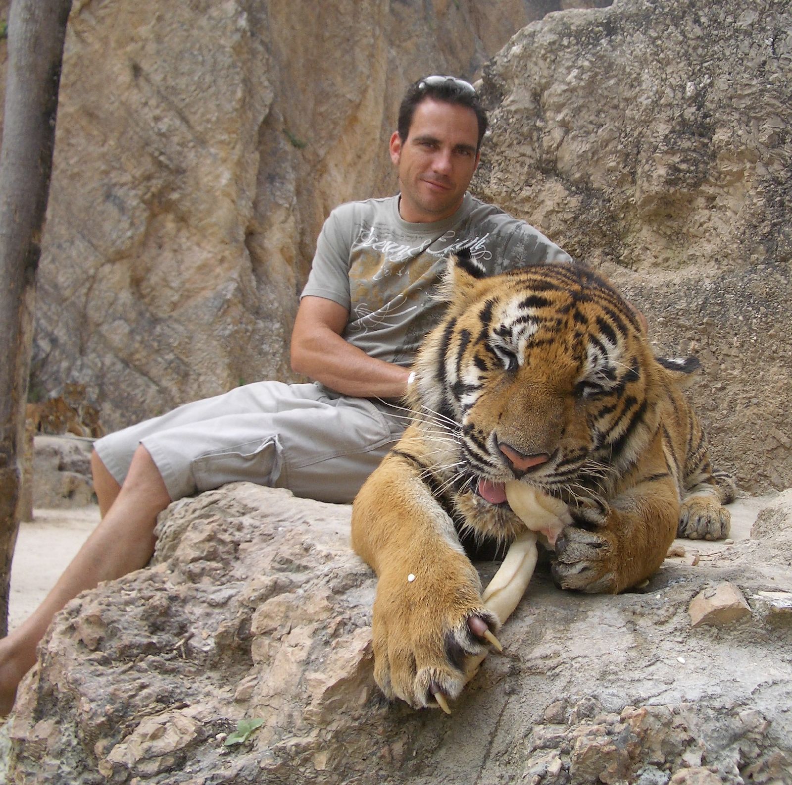 a man sits next to a tiger on a rocky outcropping