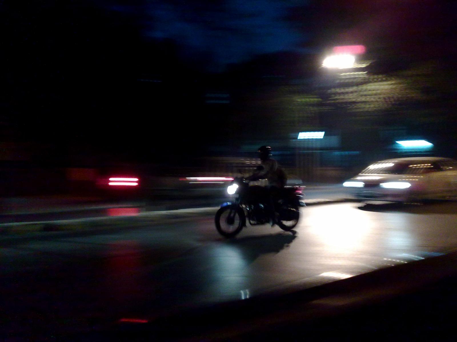 a person riding a motorcycle with a car passing behind him on the road