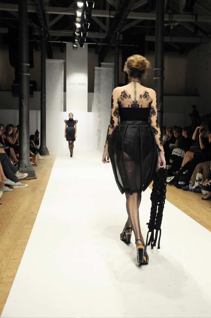 a woman walking down a runway with a black purse