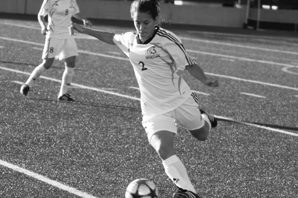 two women kicking a soccer ball on a field